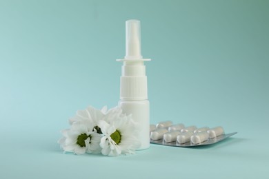 Photo of Allergy treatment. Nasal spray, pills and flowers on light blue background