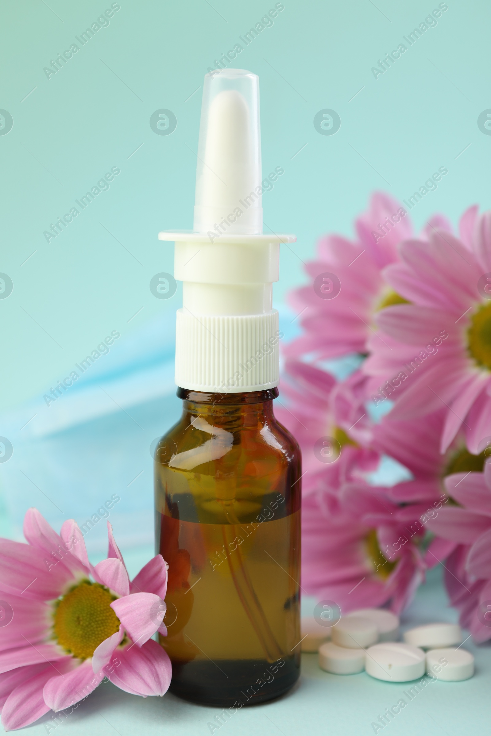 Photo of Allergy treatment. Nasal spray, pills and flowers on light blue background