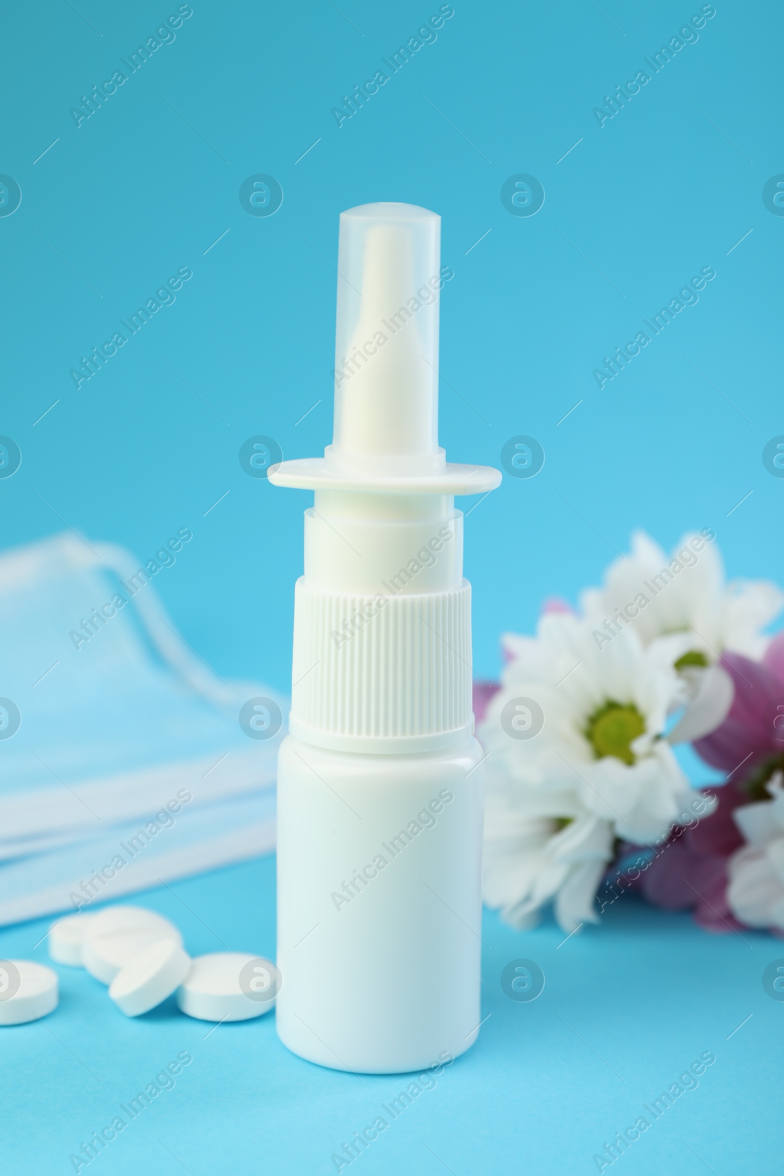 Photo of Allergy treatment. Nasal spray, pills, protective mask and flowers on light blue background, closeup