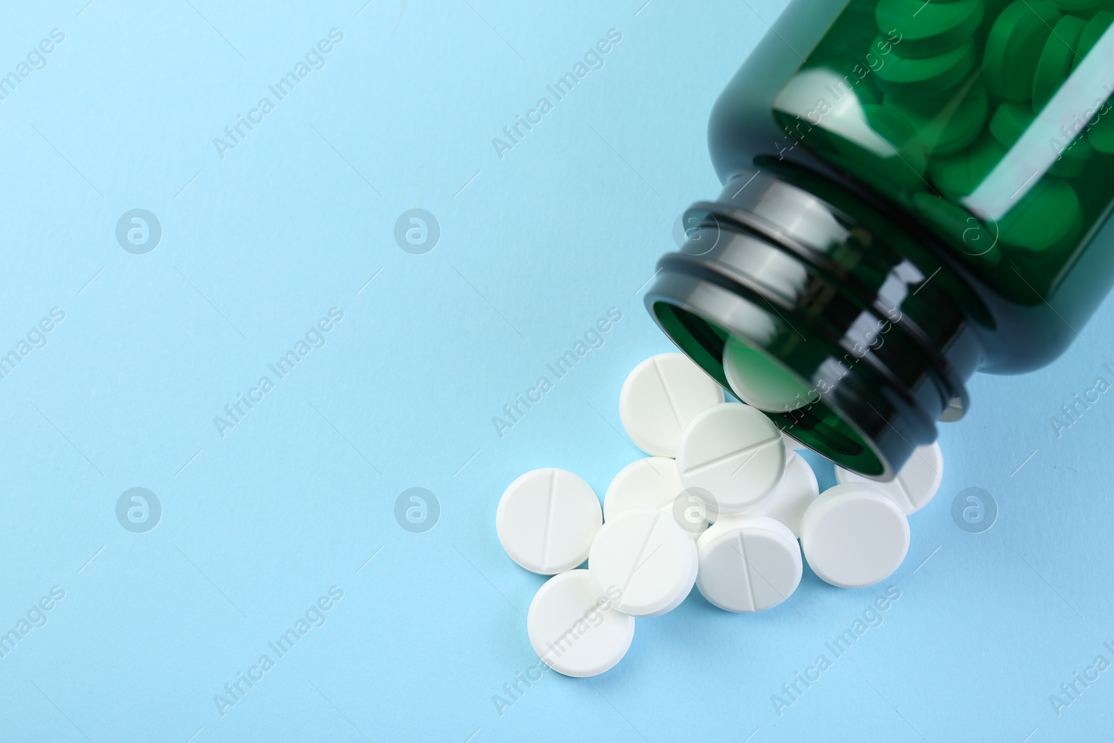 Photo of Medical bottle with antibiotic pills on light blue background, top view. Space for text