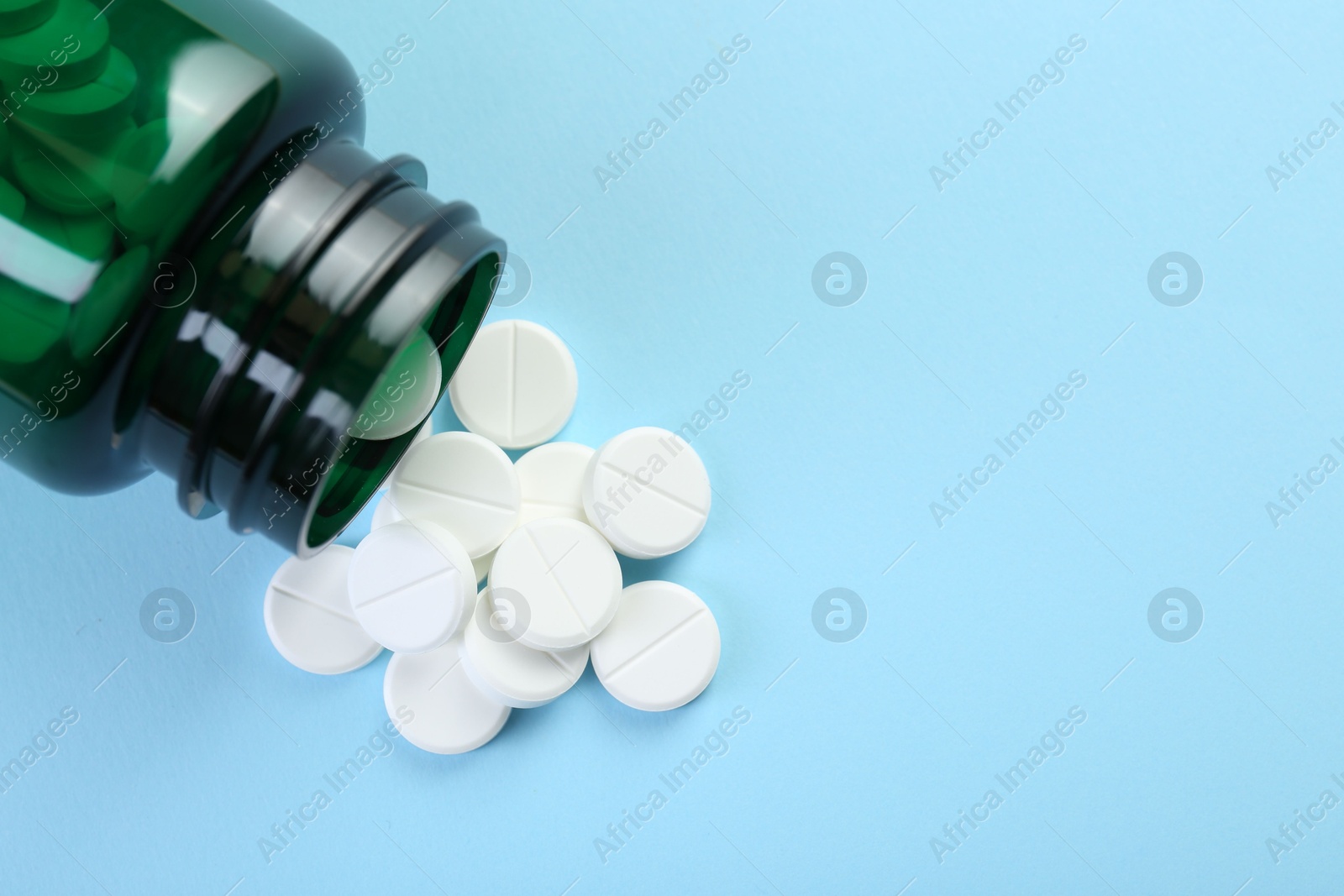 Photo of Medical bottle with antibiotic pills on light blue background, top view. Space for text