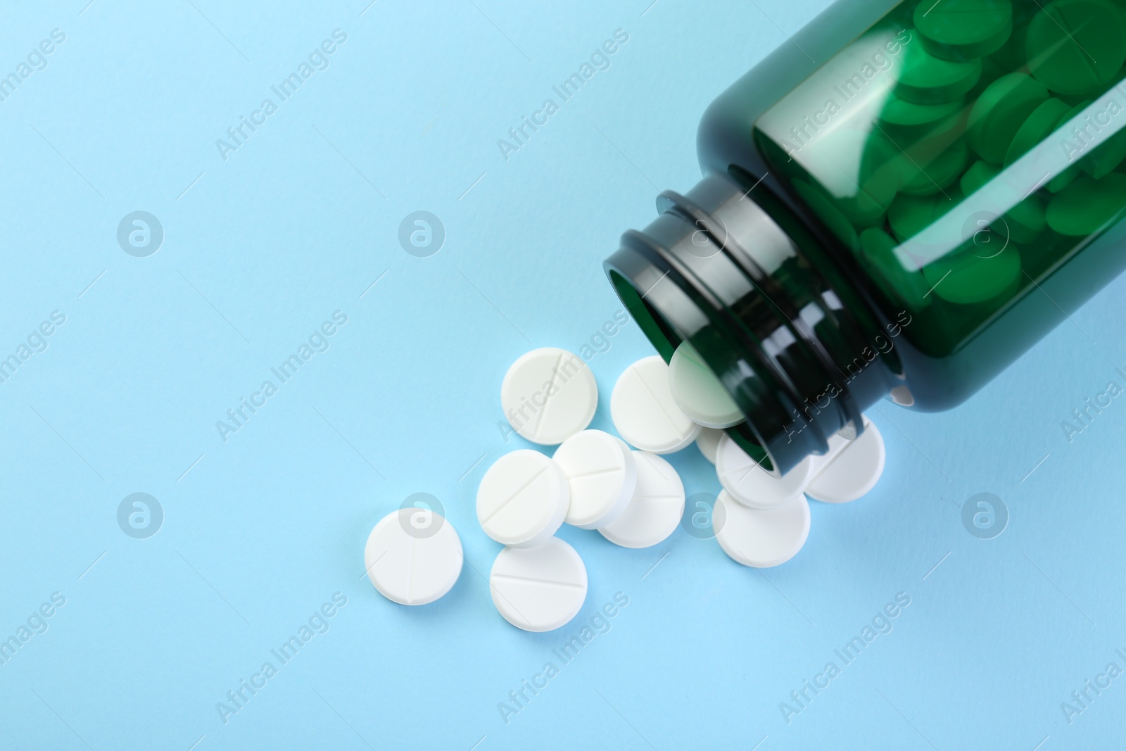 Photo of Medical bottle with antibiotic pills on light blue background, top view. Space for text