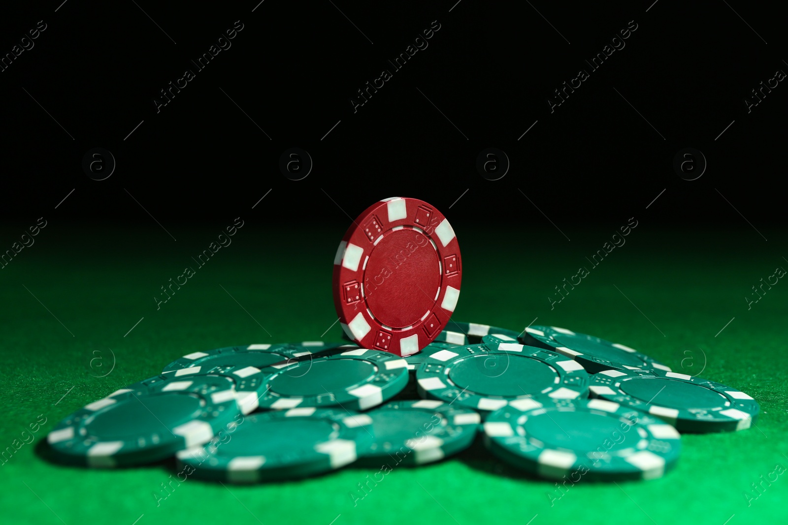 Photo of Poker chips on green table against dark background, closeup