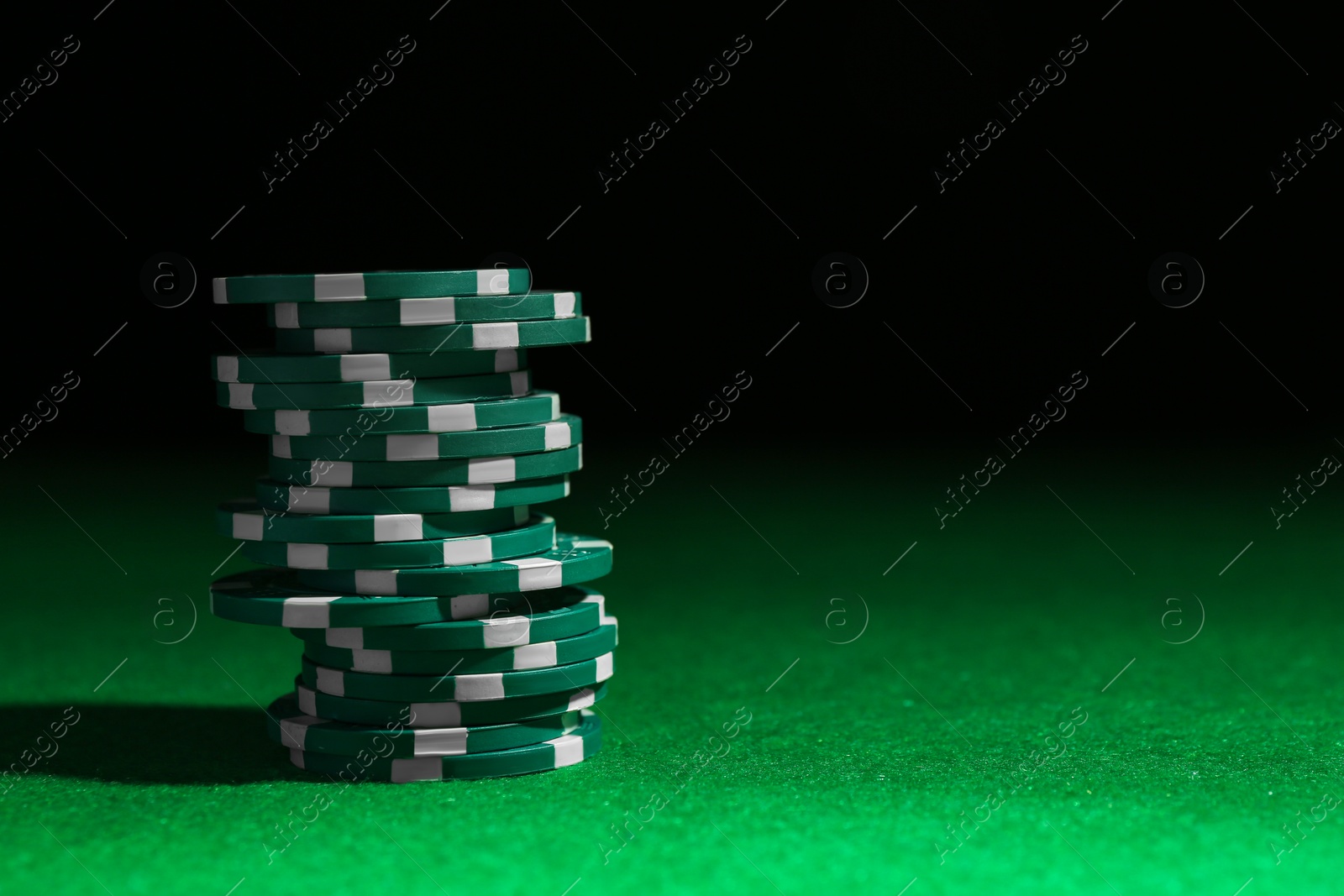 Photo of Stack of poker chips on green table against dark background, closeup. Space for text