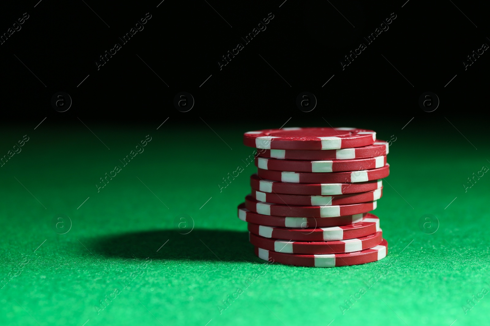 Photo of Stack of poker chips on green table against dark background, closeup. Space for text