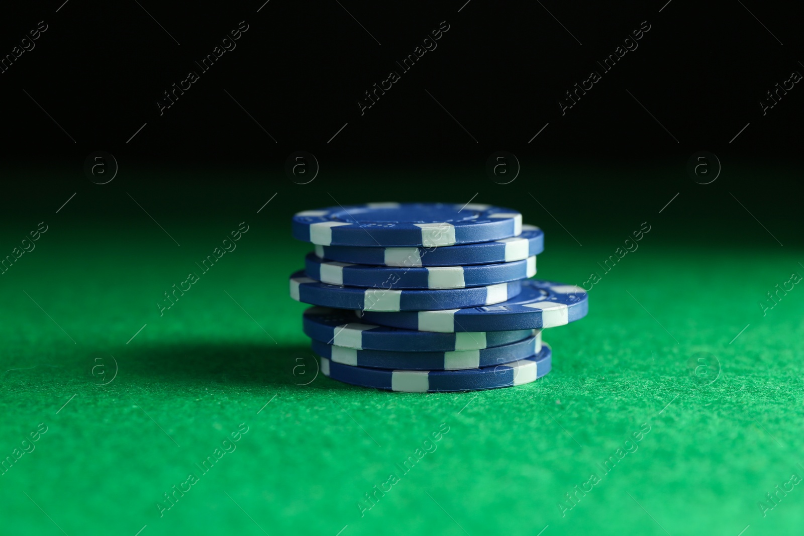 Photo of Stack of poker chips on green table against dark background, closeup