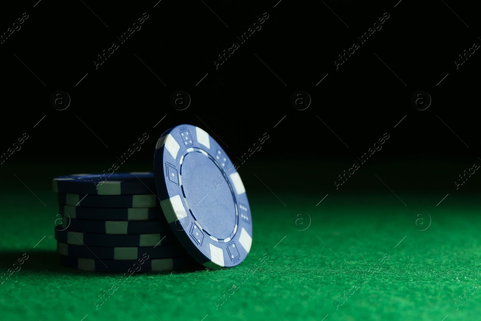 Photo of Stack of poker chips on green table against dark background, closeup. Space for text