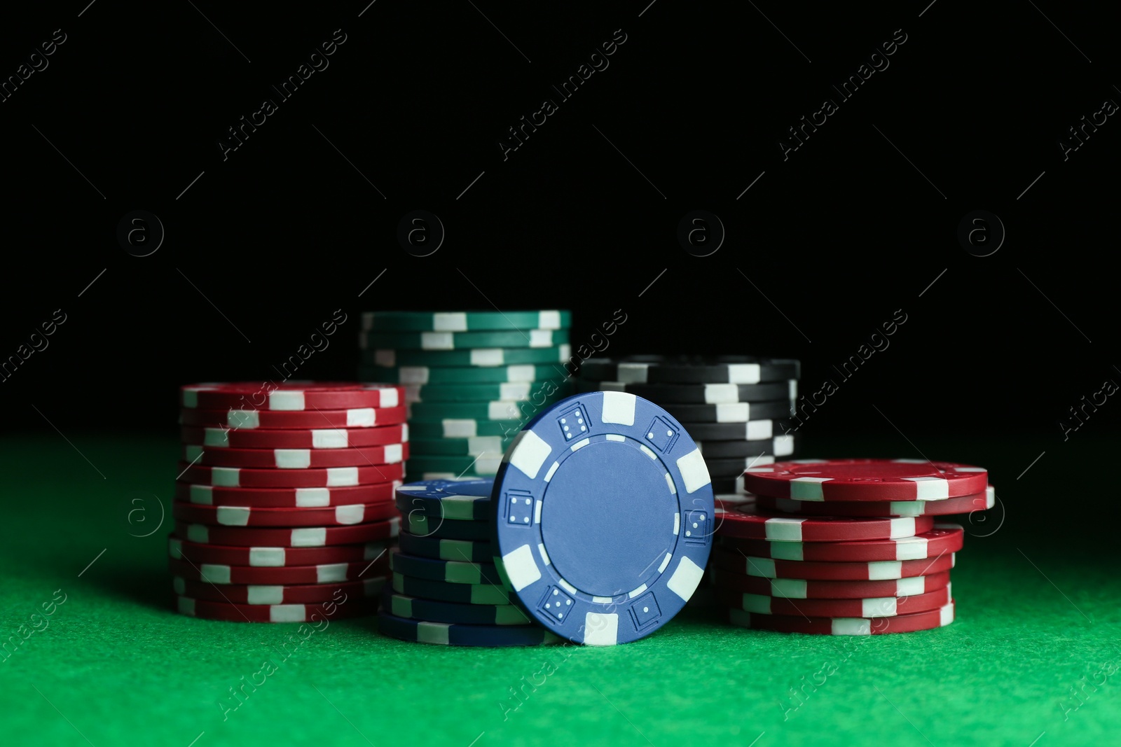 Photo of Poker chips on green table against dark background, closeup