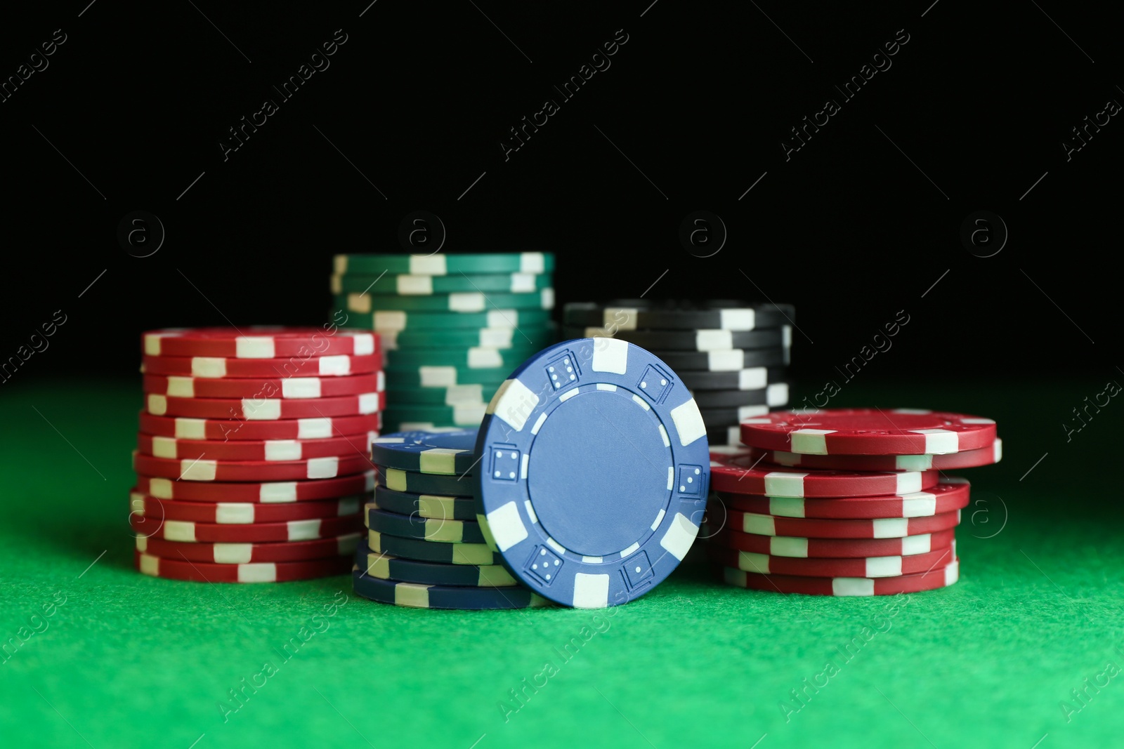 Photo of Poker chips on green table against dark background, closeup