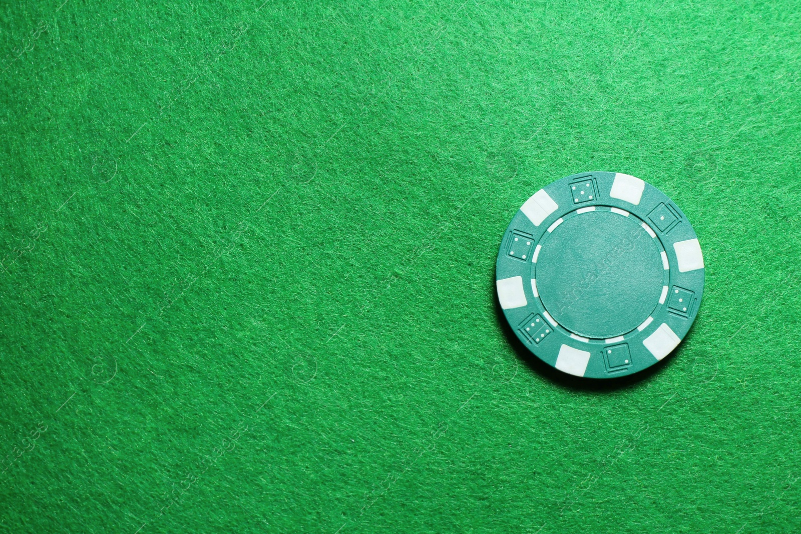 Photo of Poker chip on green table, top view. Space for text