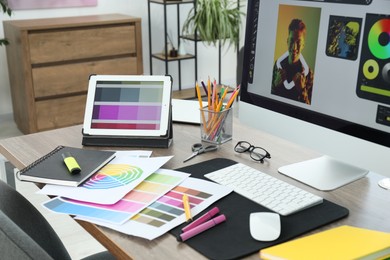 Photo of Designer's workplace with computer, tablet, color palettes and stationery on wooden table indoors