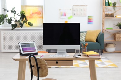 Photo of Designer's workplace with computer, tablet, color palette and stationery on wooden table indoors