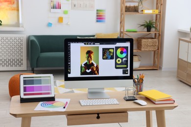 Photo of Designer's workplace with computer, tablet, color palette and stationery on wooden table indoors