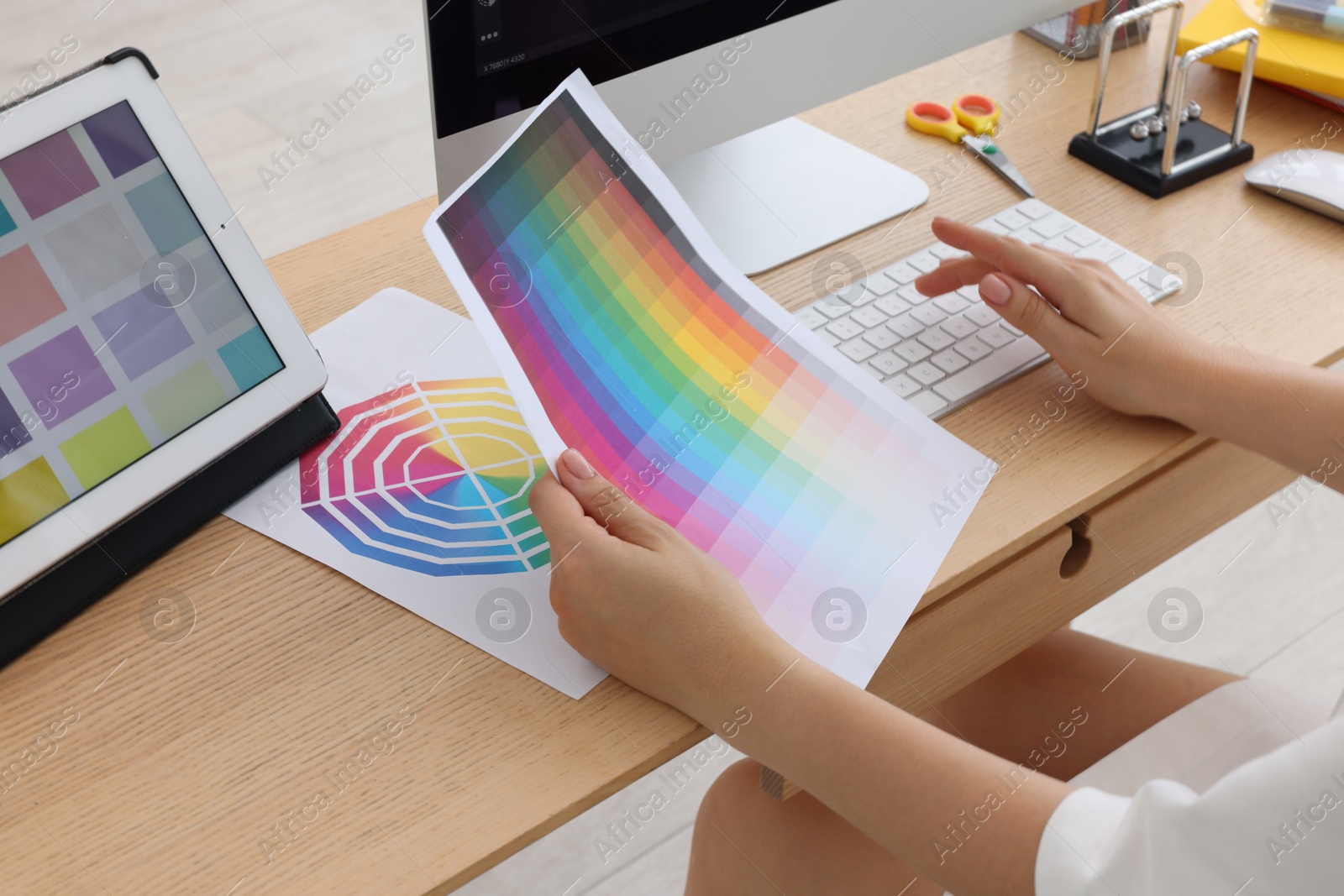 Photo of Designer with color palette working on computer at wooden table indoors, closeup