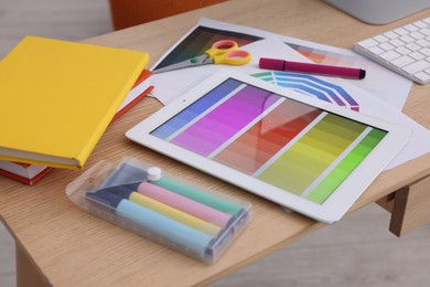 Photo of Designer's workplace with tablet, color palette and stationery on wooden table, closeup