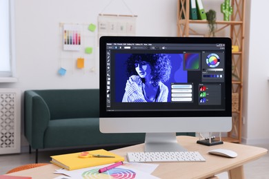 Photo of Designer's workplace with computer, color palette and stationery on wooden table indoors