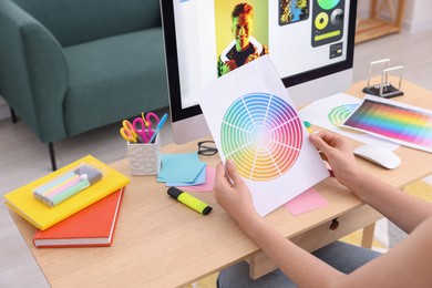 Photo of Designer with color palette working at wooden table indoors, closeup