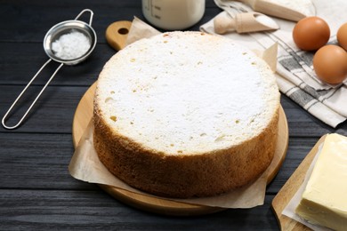 Photo of Delicious sponge cake and ingredients on black wooden table