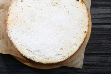 Photo of Delicious sponge cake with powdered sugar on black wooden table, top view