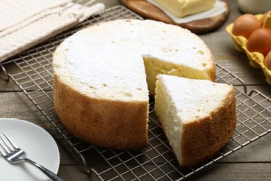 Photo of Delicious cut sponge cake, fork and ingredients on wooden table