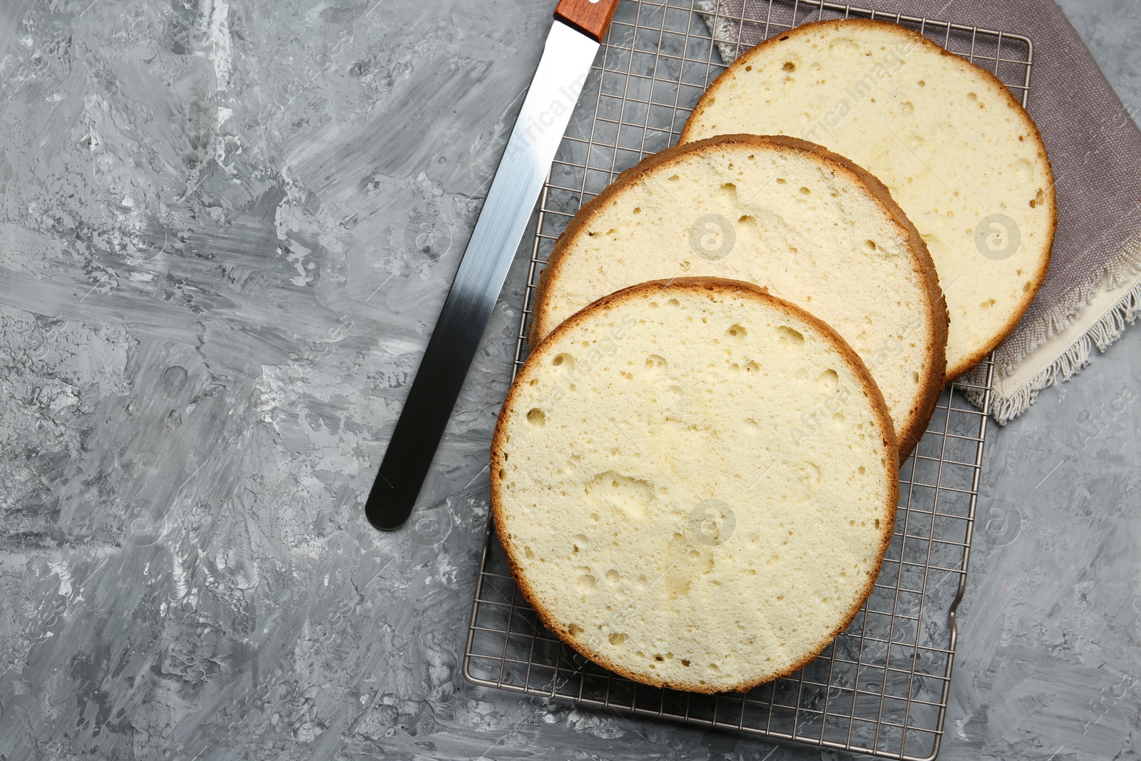 Photo of Delicious cut sponge cake and knife on grey textured table, flat lay