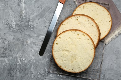 Photo of Delicious cut sponge cake and knife on grey textured table, flat lay