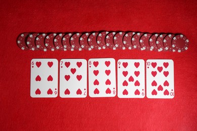 Playing cards and poker chips on red table, flat lay