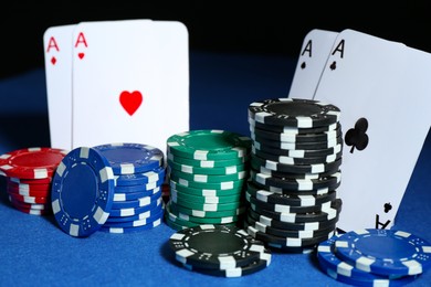 Photo of Playing cards and poker chips on blue table against dark background, closeup