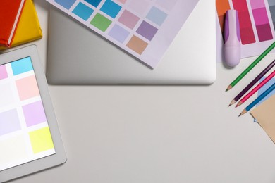 Photo of Designer's workplace with tablet, laptop, palettes and stationery on white table, flat lay