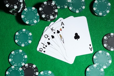 Photo of Playing cards and poker chips on green table, flat lay