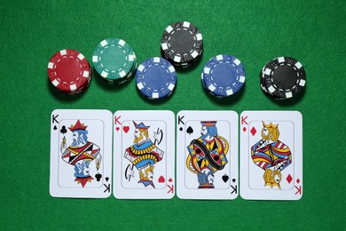 Photo of Playing cards and poker chips on green table, flat lay