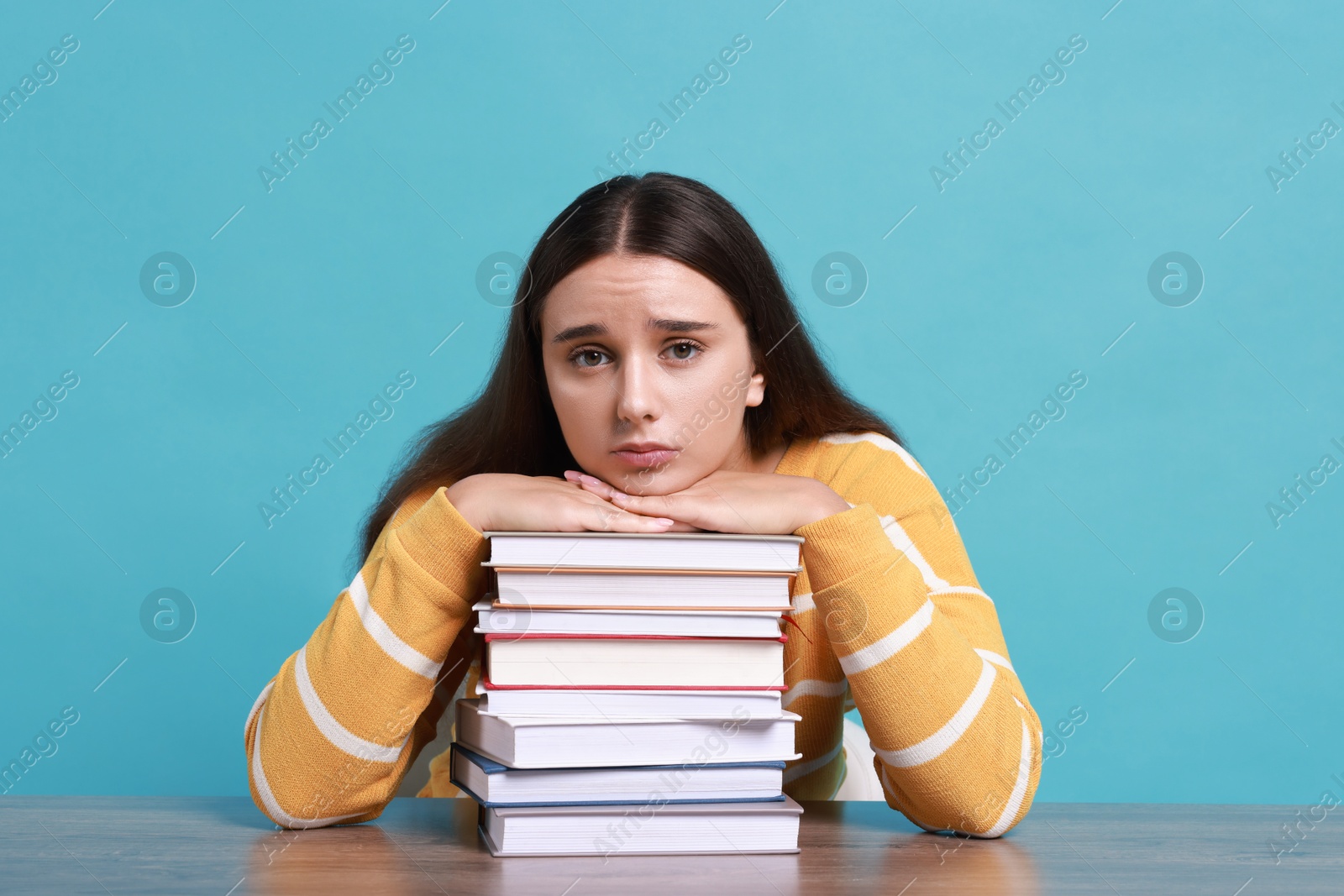 Photo of Young student with books having stress before exam at table against light blue background