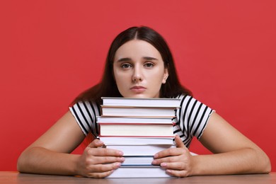 Photo of Young student with stack of books having stress before exam at table against red background