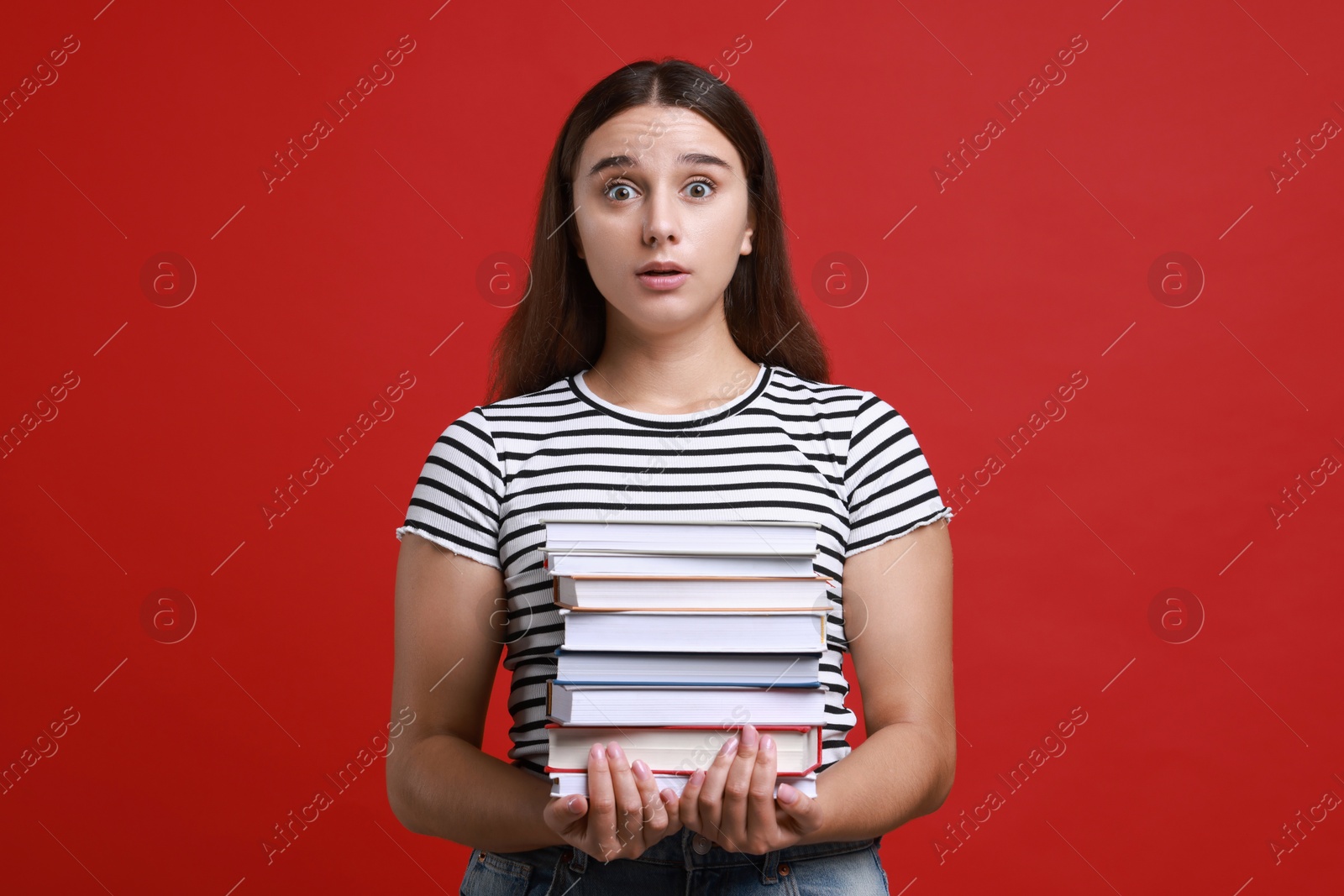 Photo of Stressful student with stack of books before exam on red background