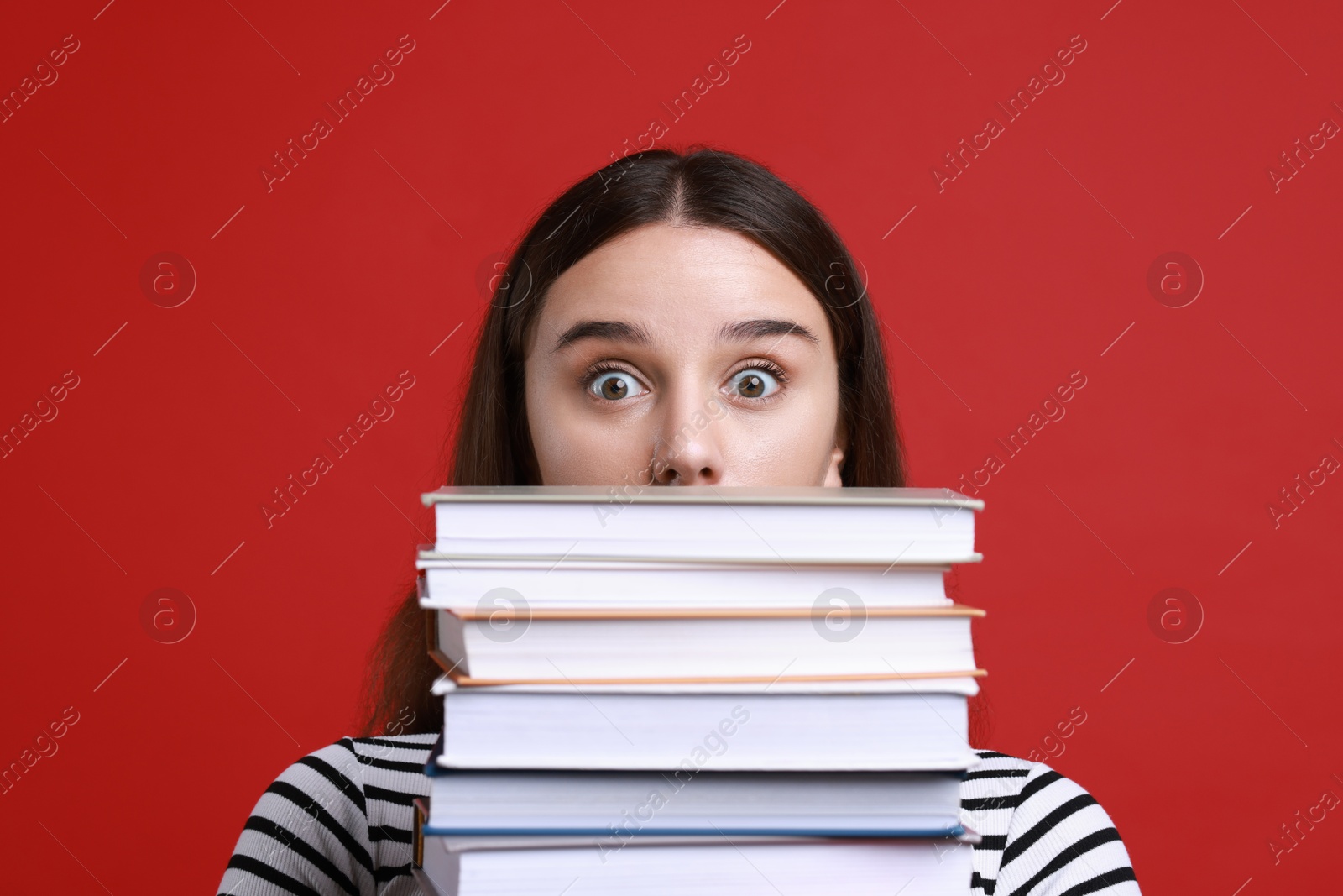 Photo of Stressful student with stack of books before exam on red background, closeup