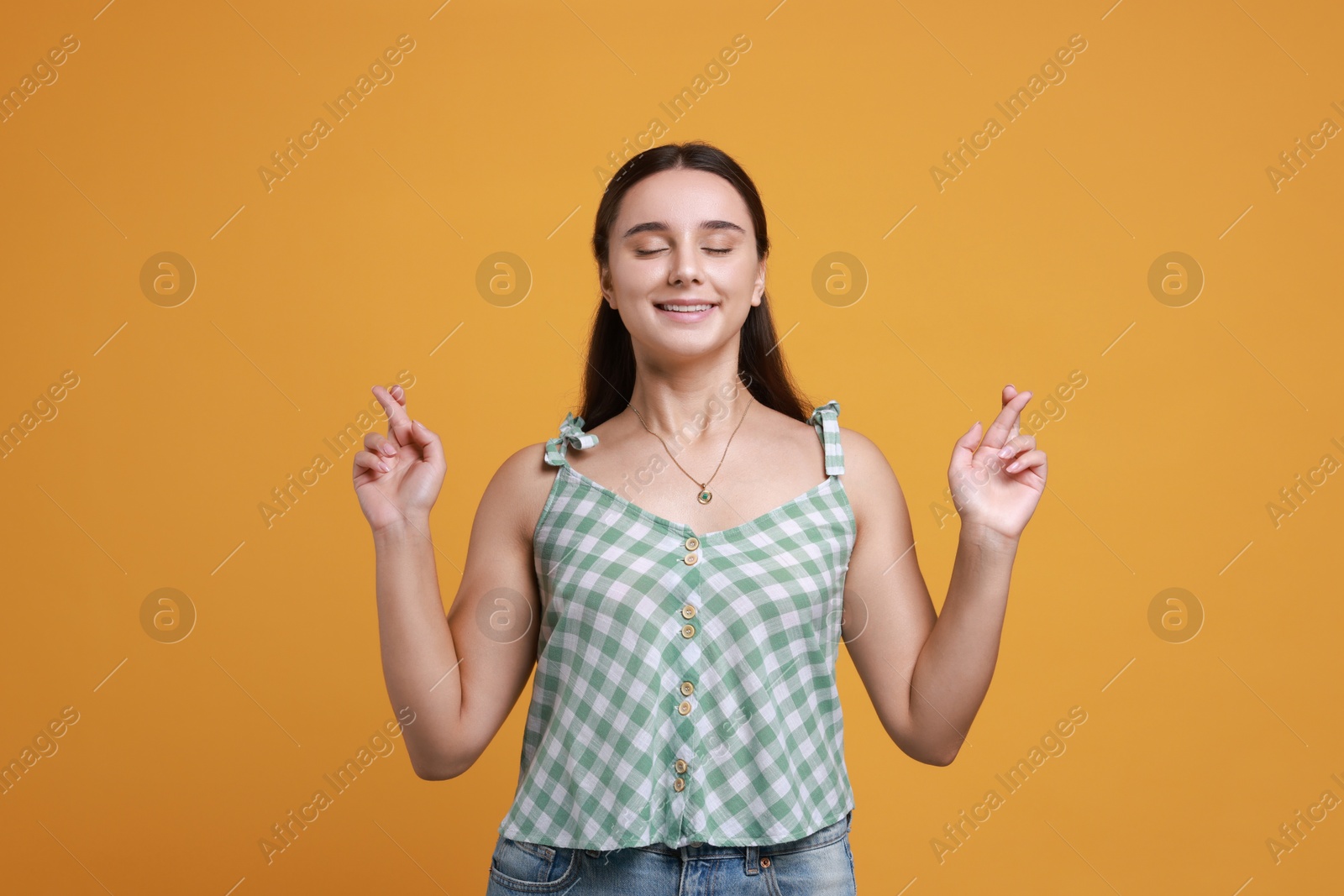 Photo of Excited young student crossing fingers on orange background. Hope for good exam result