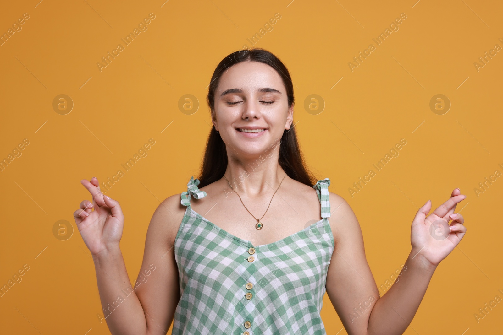 Photo of Excited young student crossing fingers on orange background. Hope for good exam result