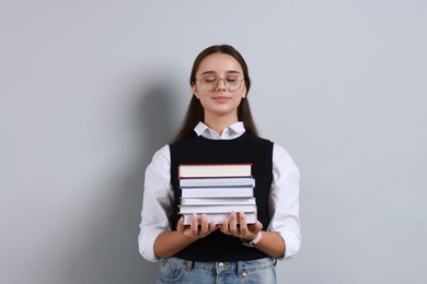 Photo of Young student with stack of books on grey background