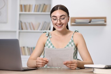 Photo of Happy student reading her good exam result at table indoors