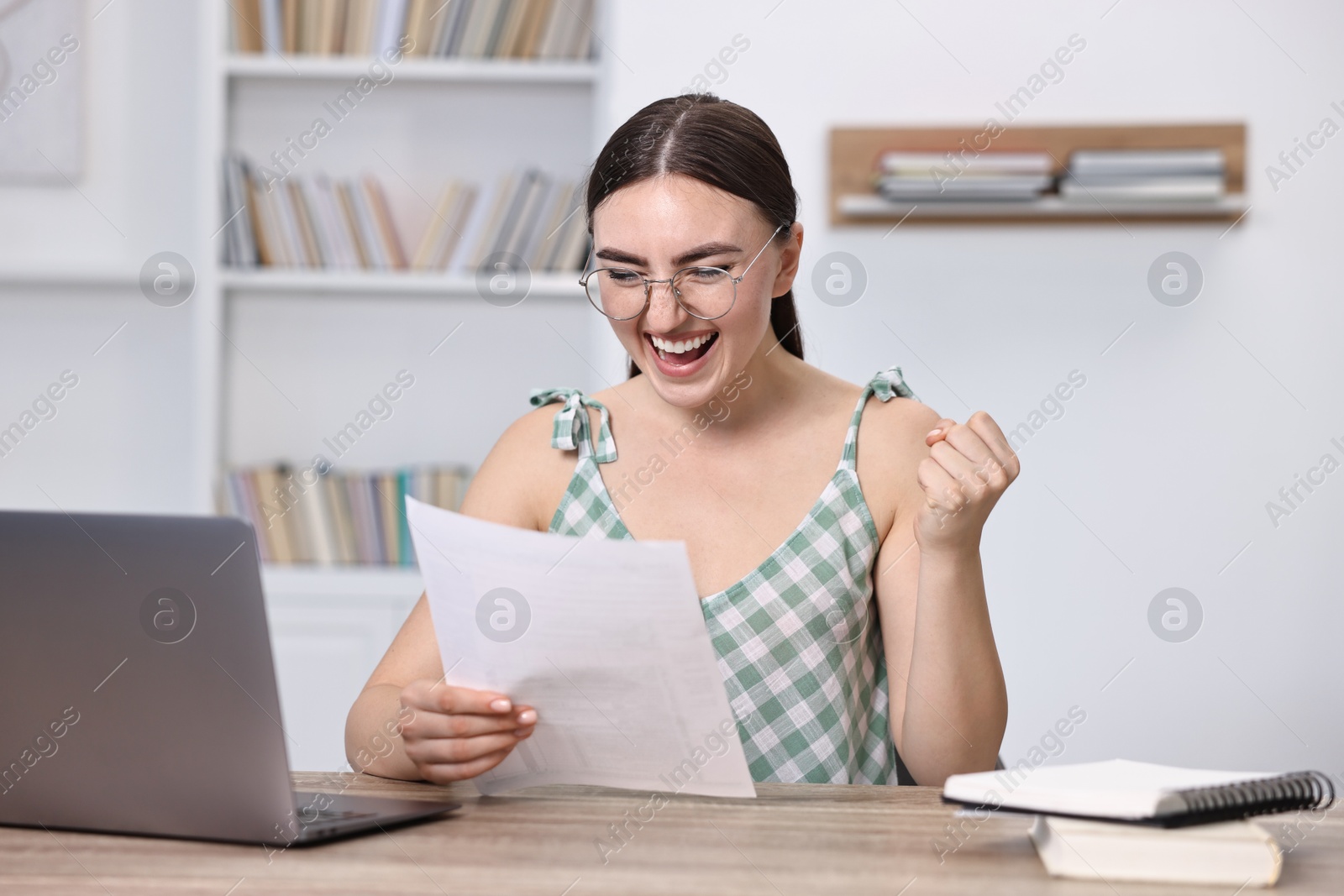 Photo of Happy student reading her good exam result at table indoors