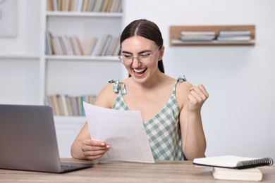 Photo of Happy student reading her good exam result at table indoors