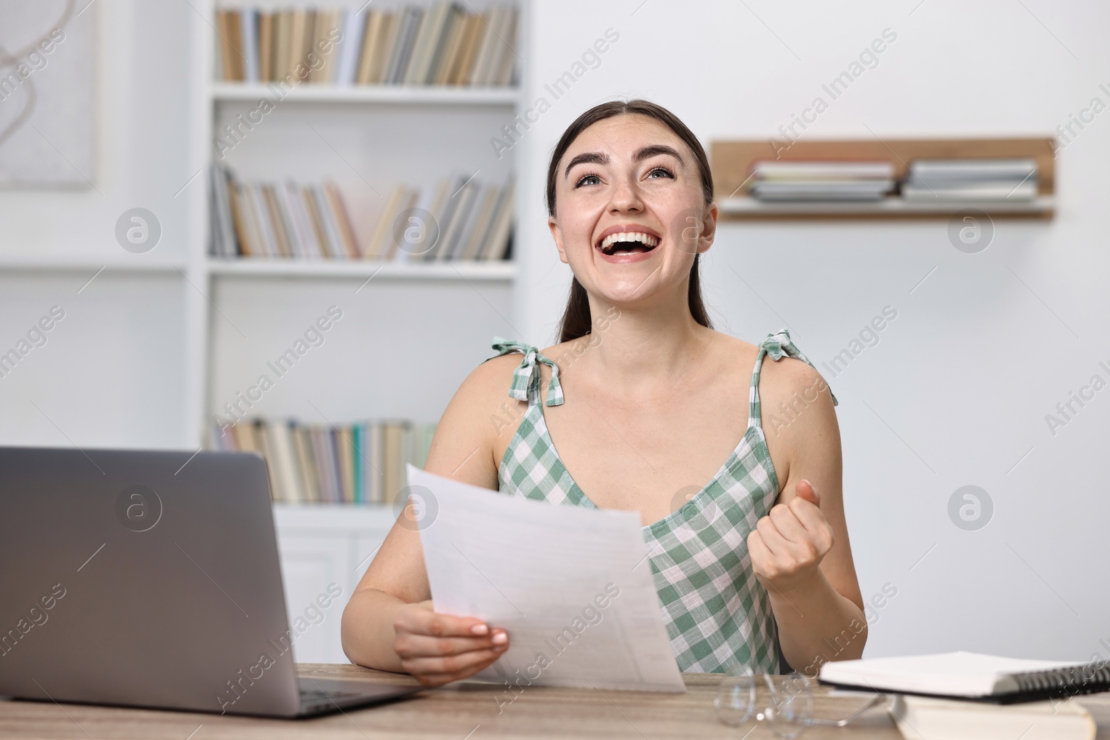 Photo of Happy student reading her good exam result at table indoors