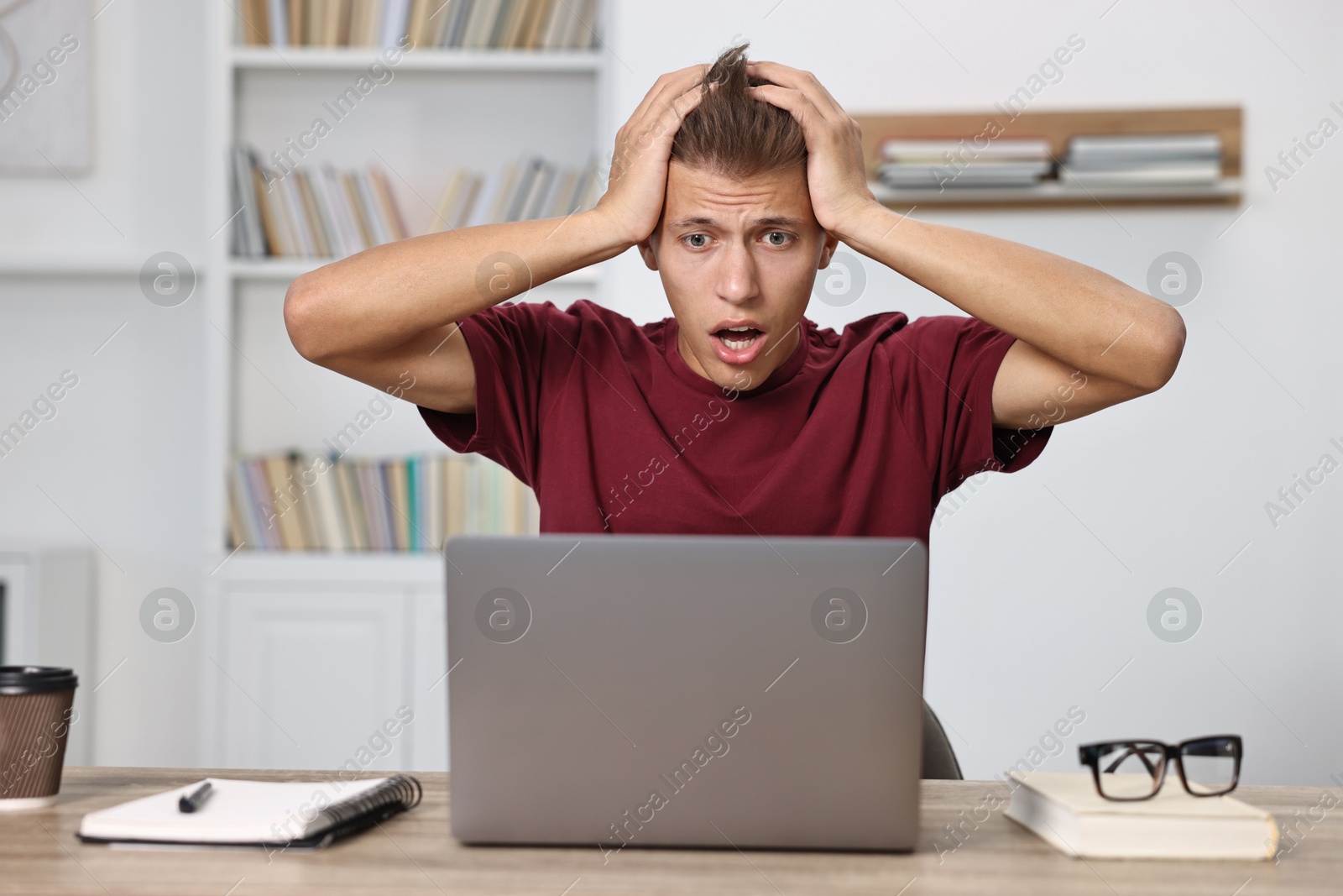 Photo of Overwhelmed student before exam at table with laptop indoors