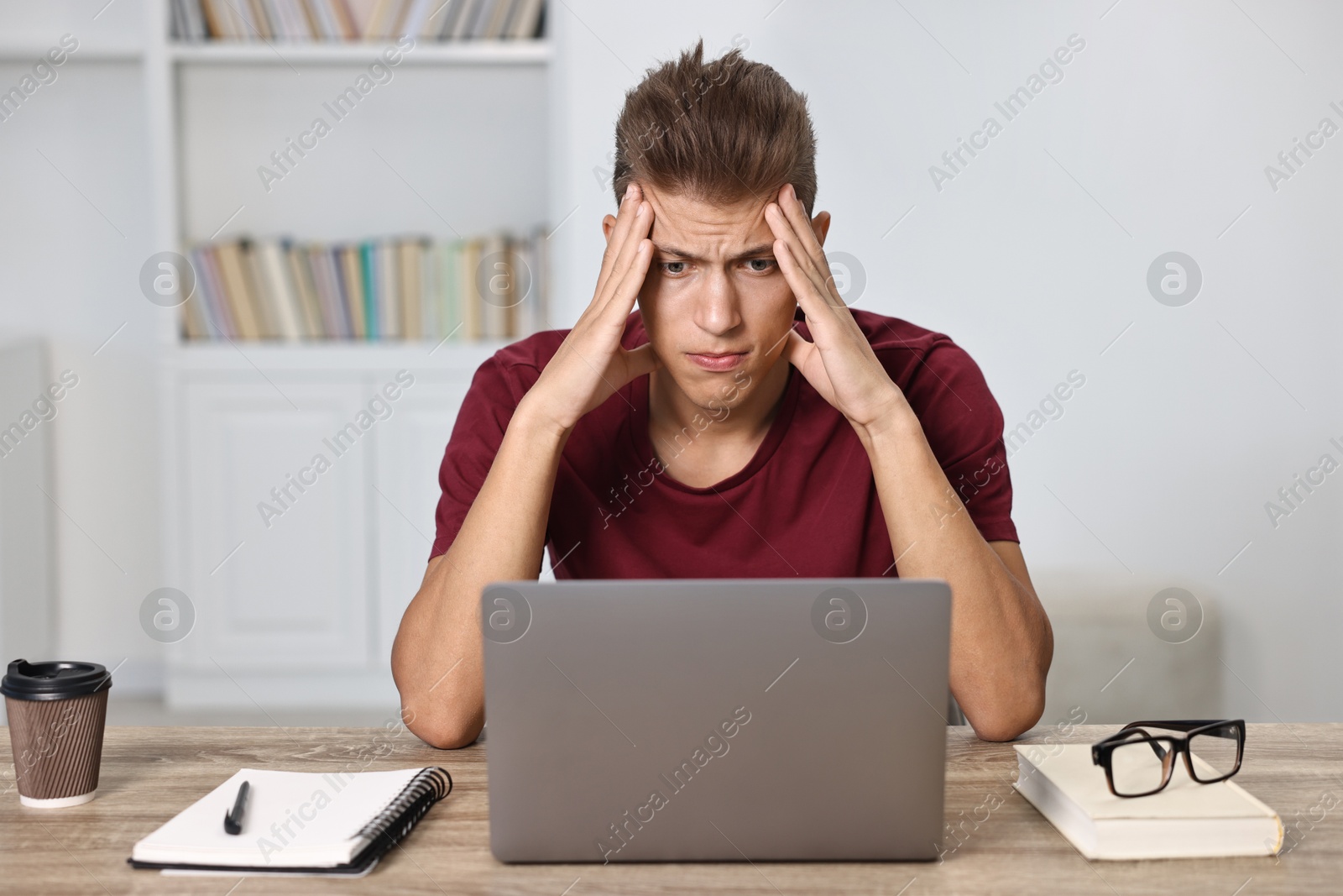 Photo of Tired student preparing for exam with laptop at table indoors