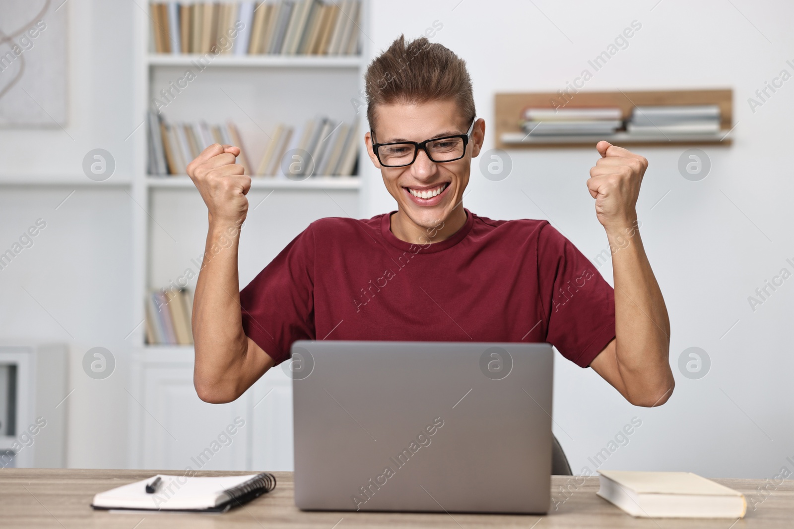 Photo of Student feeling happy about his good exam result at table with laptop indoors