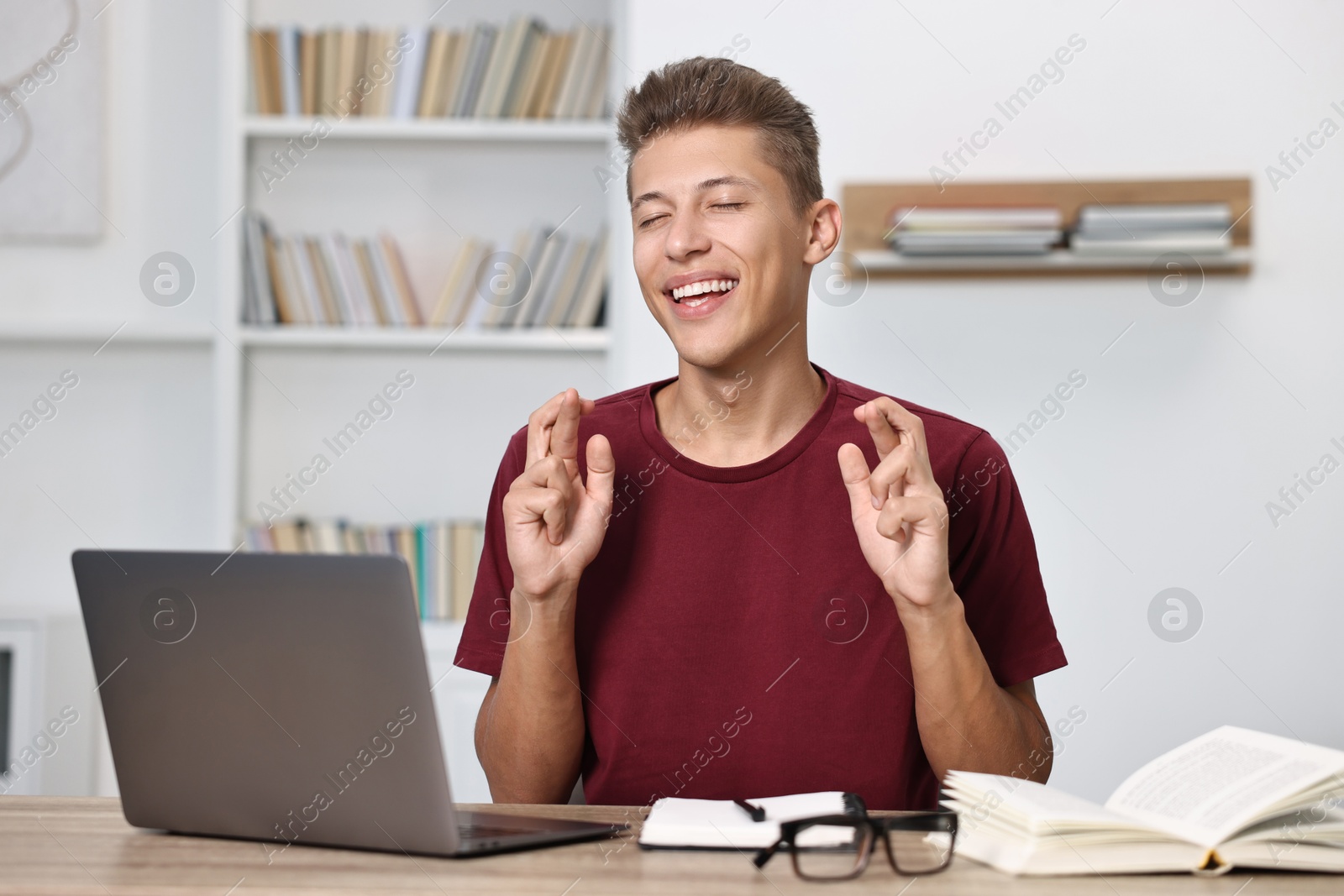 Photo of Student with crossed fingers at table with laptop indoors. Hope for good exam result