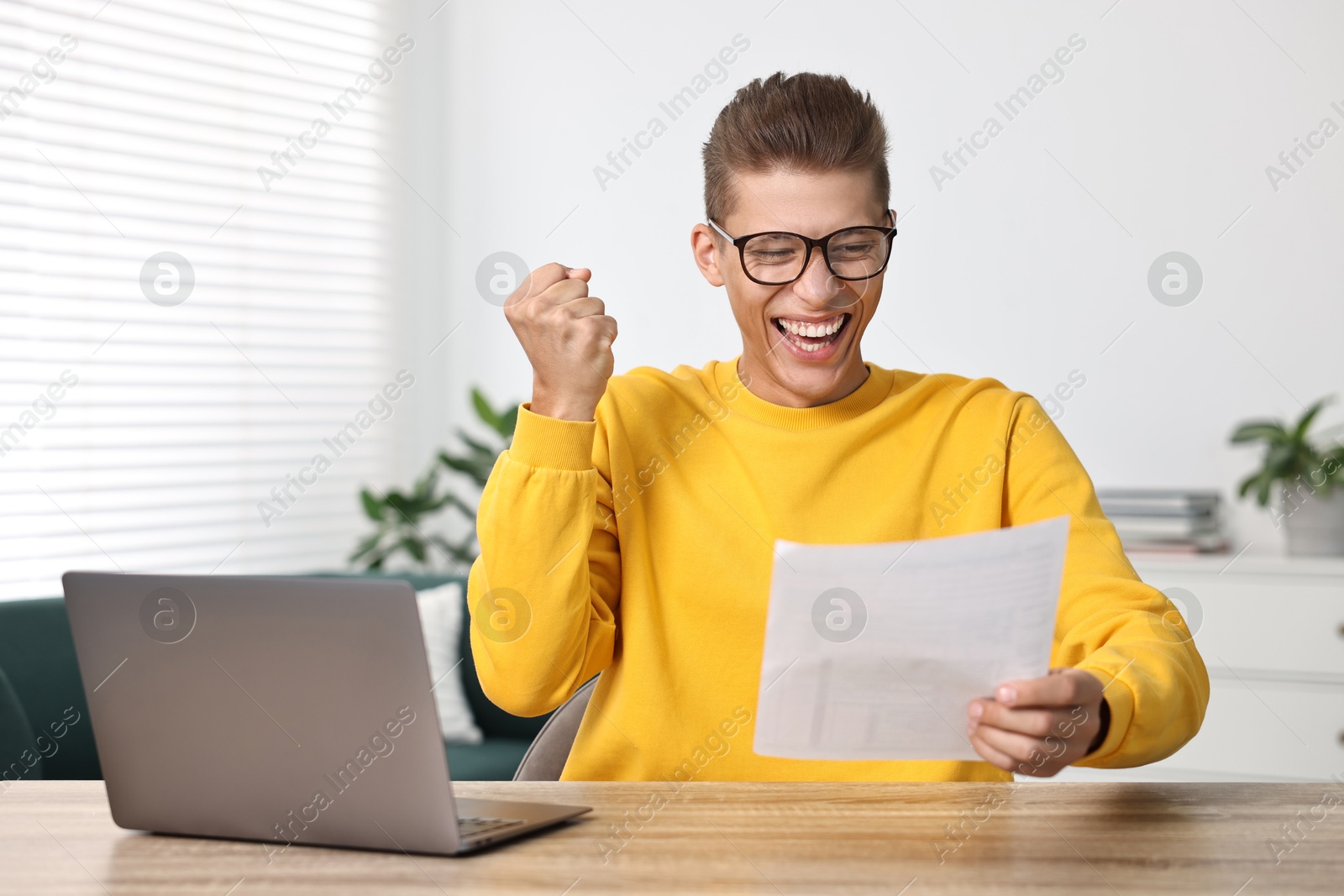 Photo of Happy student reading his good exam result at table indoors