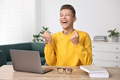 Student feeling happy about his good exam result at table with laptop indoors