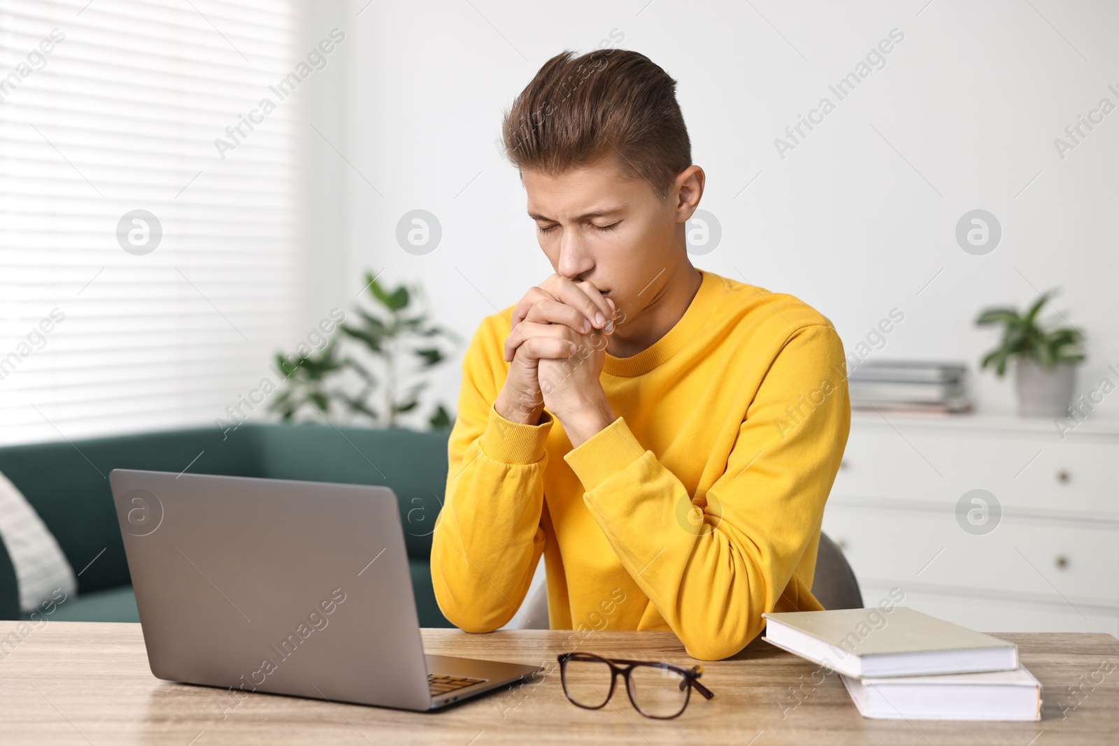 Photo of Student praying for good exam result at table with laptop indoors