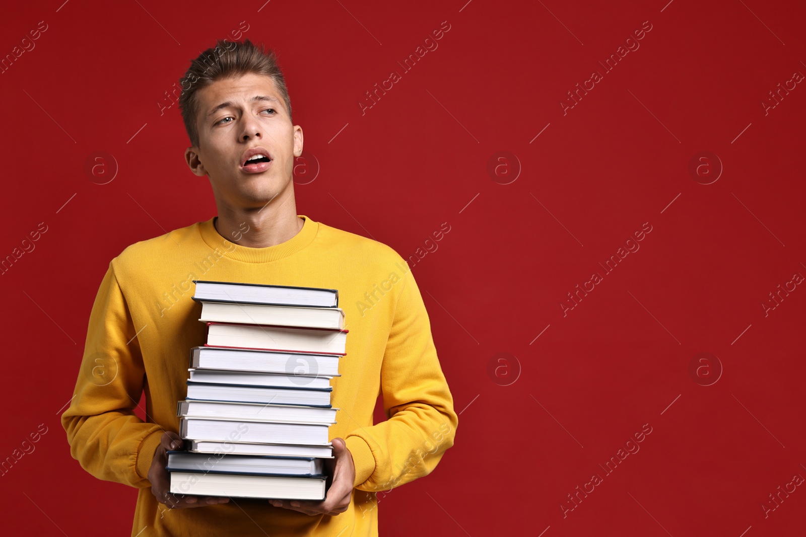 Photo of Tired student with stack of books having stress before exam on red background. Space for text